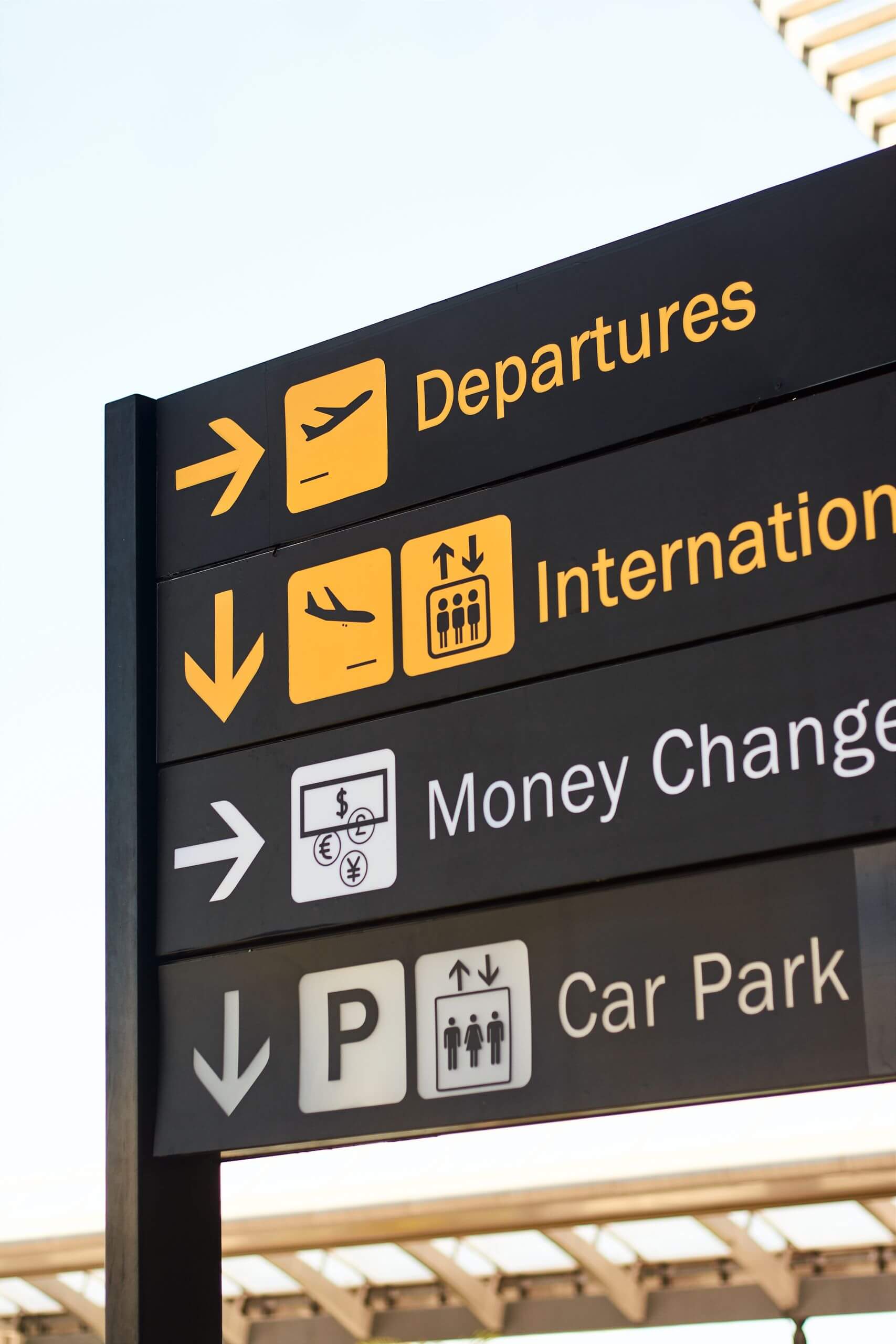 Close-up of airport direction signs for departures, international, money change, and car park.